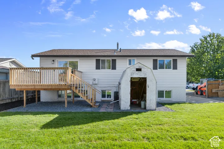 Rear exterior featuring light-toned horizontal siding, a raised wood deck with stair access, a gravel ground covering, and a detached storage structure