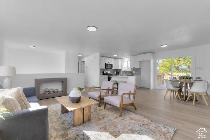 Open-concept interior featuring light-tone wood-finish flooring, recessed lighting, and kitchen cabinetry with a neutral tile backsplash
