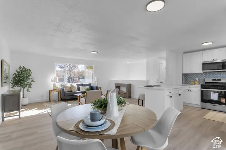 Open-concept living space featuring wood-finish flooring, a kitchen with white cabinetry, a center island with a quartz countertop, and a patterned tile backsplash