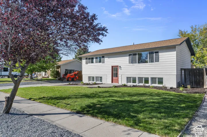 Two-story residence featuring light-toned horizontal siding, a lower-level brick facade, a composition shingle roof, and a front lawn with mature landscaping