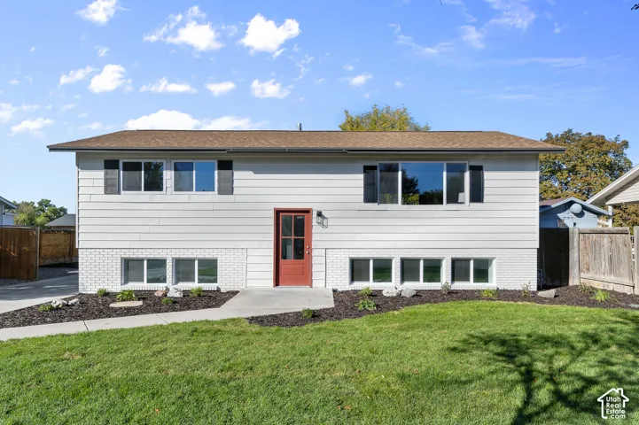 Split-level exterior featuring light horizontal siding, white brick lower-level masonry, a red-painted door, dark window shutters, and a concrete walkway