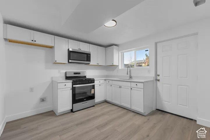 Kitchen featuring white shaker-style cabinetry, solid-surface countertops, wood-finish flooring, stainless steel appliances, and an undermount sink with a pull-down faucet