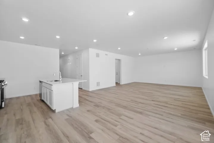 Open concept floor plan with wood-finish flooring, recessed lighting, and a central island featuring a stone countertop and undermount sink