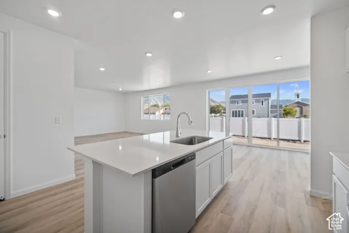 Kitchen island featuring a stone-composite countertop, stainless steel undermount sink, gooseneck faucet, and integrated stainless steel dishwasher, complemented by recessed ceiling lighting and wood-finish flooring