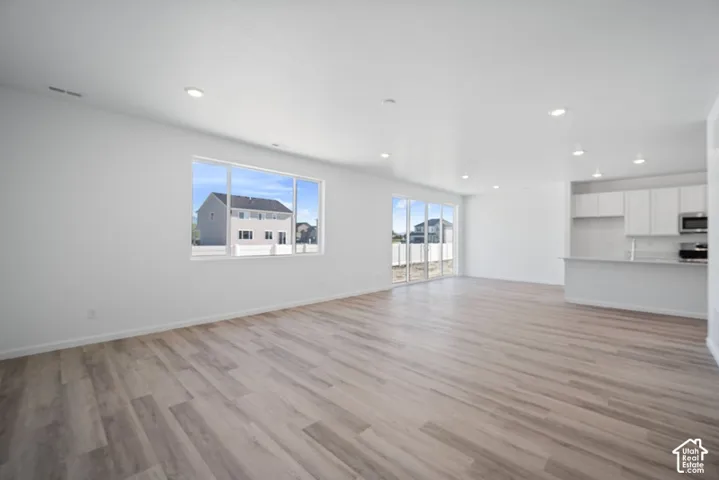 Open-concept space featuring wood-finish flooring, recessed lighting, expansive windows, glass patio doors, and white built-in kitchen cabinetry