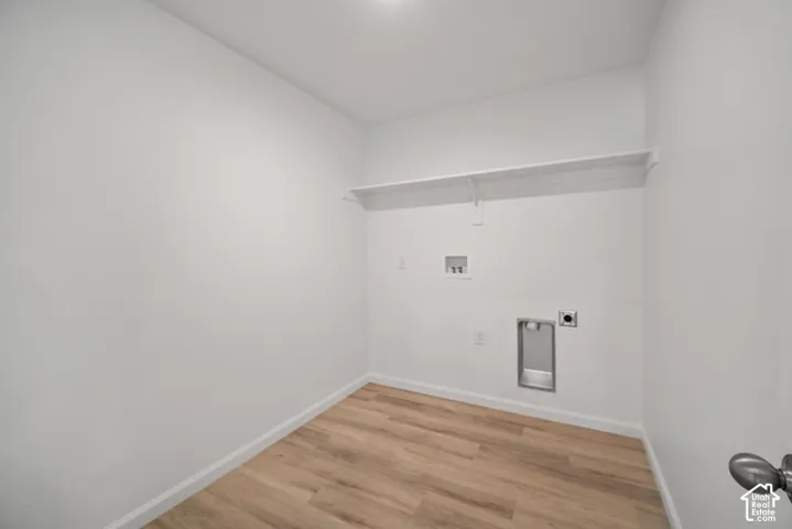 Utility space featuring wood-finish flooring, a wall-mounted shelving unit, and dedicated hookups for laundry appliances