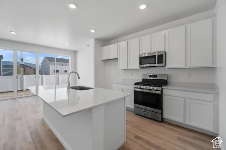 Kitchen featuring white cabinetry, quartz countertops, a central island with a stainless steel sink, stainless steel appliances, and wood-finish flooring