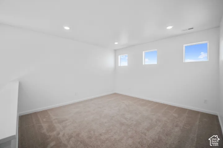 Neutral-toned carpeted flooring, white walls, and three high-positioned square windows complemented by recessed lighting