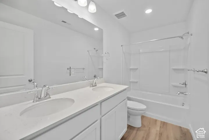 Double vanity featuring a light-toned countertop with dual integrated sinks and polished chrome fixtures, complemented by white cabinetry, a full-width vanity mirror, and wood-finish flooring