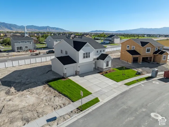 Two-story exterior featuring white horizontal siding, a multi-gabled roofline, a three-car garage, and stone veneer accents, set against a mountain backdrop