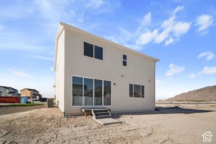 Two-story exterior featuring a light-toned stucco facade, sliding glass door, and stepped exterior platform with mountain backdrop