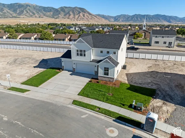 Two-story residence featuring horizontal siding, a multi-gabled asphalt shingle roof, a stone masonry facade accent, an attached three-car garage, and mountain backdrop