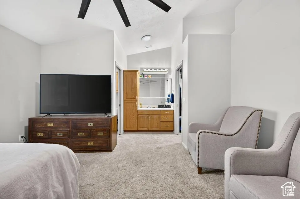 Vaulted ceiling with integrated black ceiling fan, neutral carpeting, and built-in wood cabinetry featuring a mirror-fronted vanity