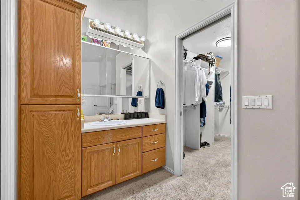 Bathroom vanity featuring wood-finish cabinetry, a white countertop with an integrated basin, a tri-fold medicine cabinet, and a multi-bulb light fixture, accompanied by a walk-in closet with built-in shelving