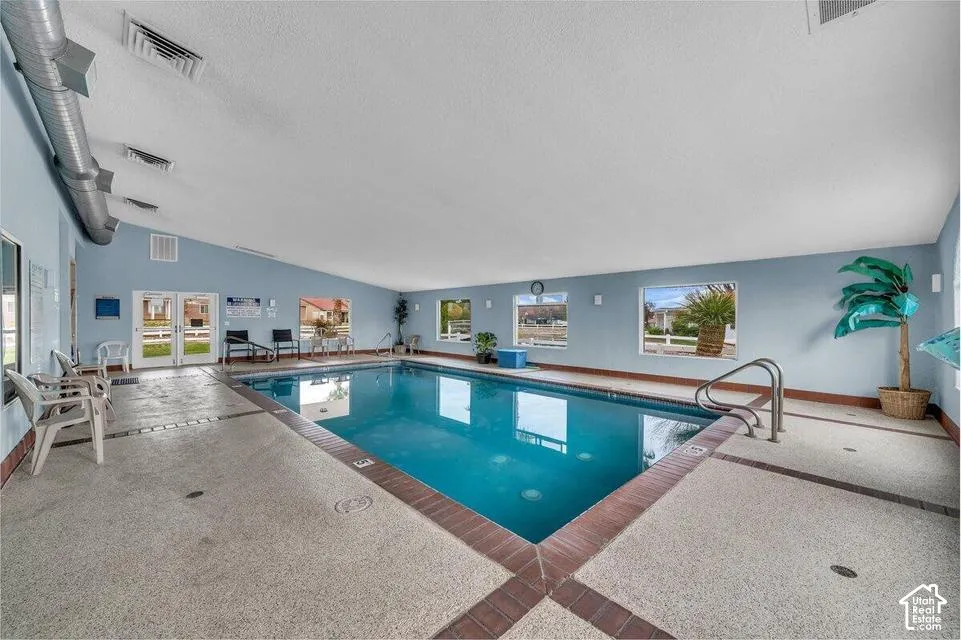 Indoor swimming pool featuring an expansive tiled deck, multiple large windows, exposed metal ductwork, and double-door exterior access