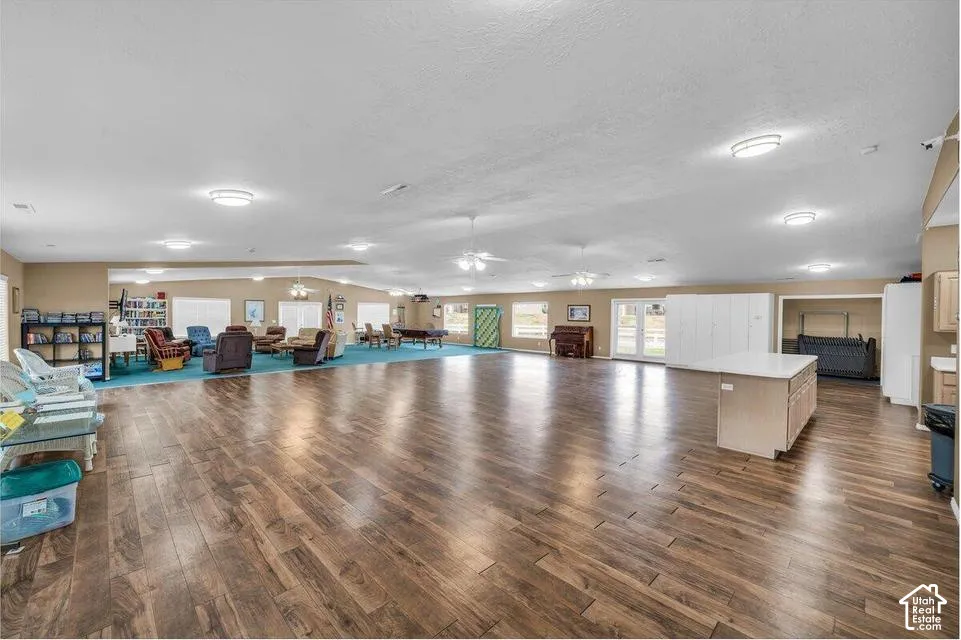 Expansive open-concept room featuring wood-finish flooring, recessed lighting, multiple ceiling fans, and an integrated kitchen island with a stone countertop