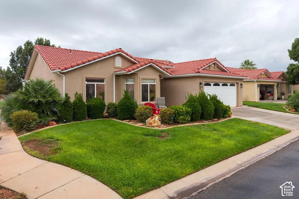 Stucco exterior residence featuring a red tile roof, multi-gable roofline, arched garage door detailing, and manicured landscaping