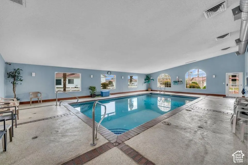 Indoor swimming pool featuring an arched ceiling, tile-trimmed concrete decking, integrated metal handrails, and large windows with arched accents