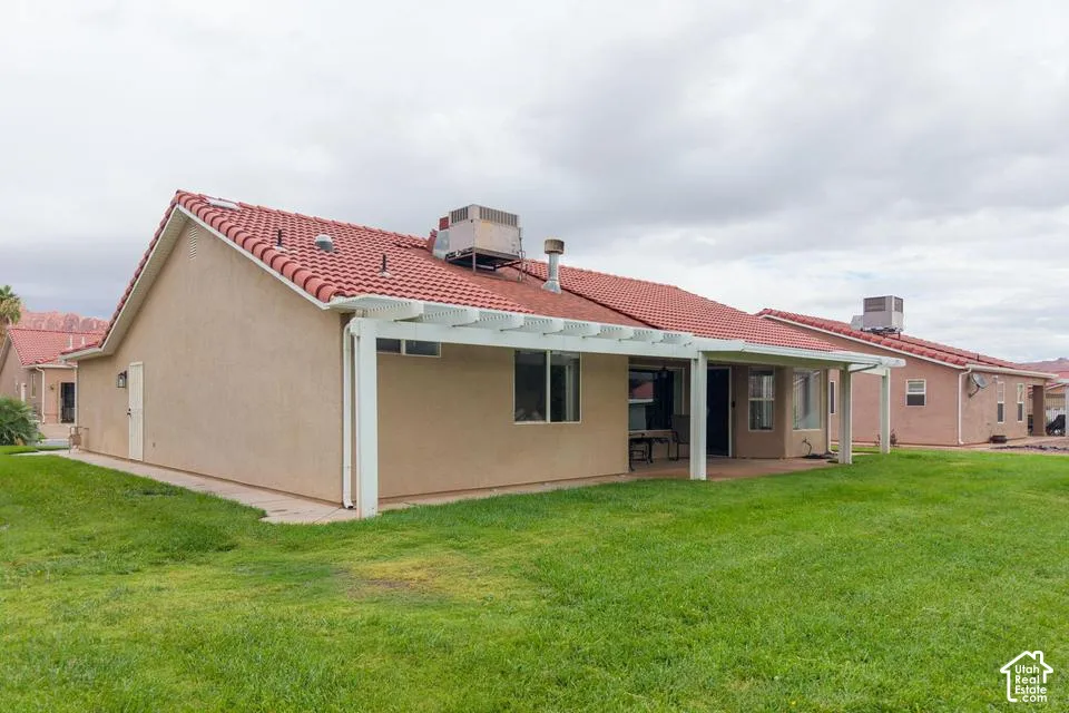 Stucco exterior featuring a red tile roof, white pergola, and landscaped lawn
