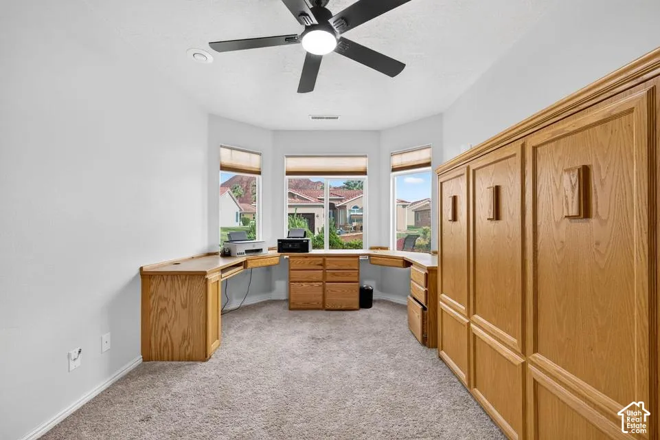 Built-in oak cabinetry with integrated desk workspace, bay window configuration, and matte black ceiling fan