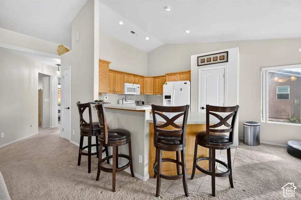 Kitchen featuring vaulted ceilings, recessed lighting, wood cabinetry, stone-finish countertops, and a breakfast bar