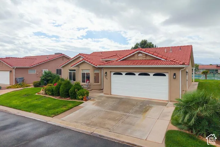 Single-story residence featuring a terracotta tile roof, stucco exterior, three-car garage with arched windows, concrete driveway, and manicured landscaping