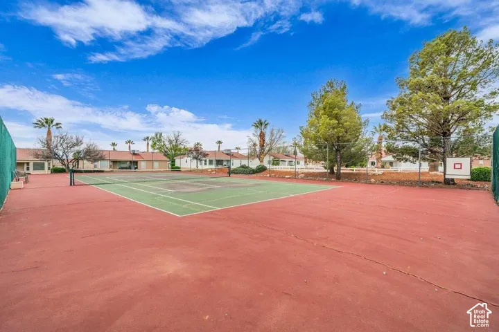 Tennis court with a paved surface, perimeter chain-link fencing, and mature trees