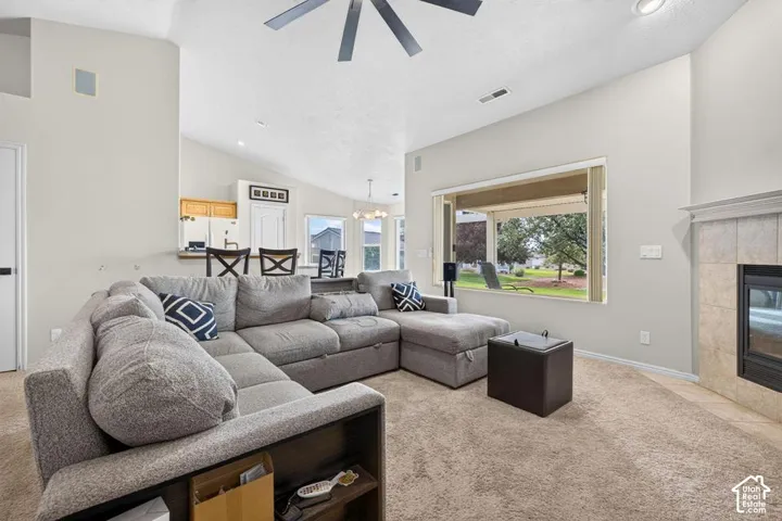 Vaulted ceilings featuring a central overhead fan, expansive picture window, and a fireplace with stone-tile surround