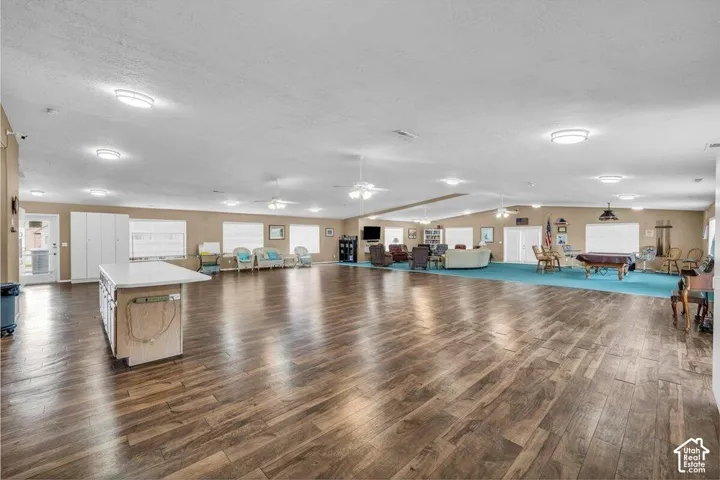 Expansive open-concept room featuring wood-finish flooring, recessed lighting, ceiling fans, and a built-in island with a white surface