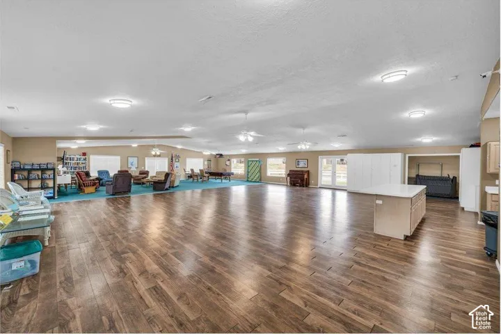 Expansive open-concept room featuring wood-finish flooring, recessed lighting, multiple ceiling fans, and an integrated kitchen island with a stone countertop
