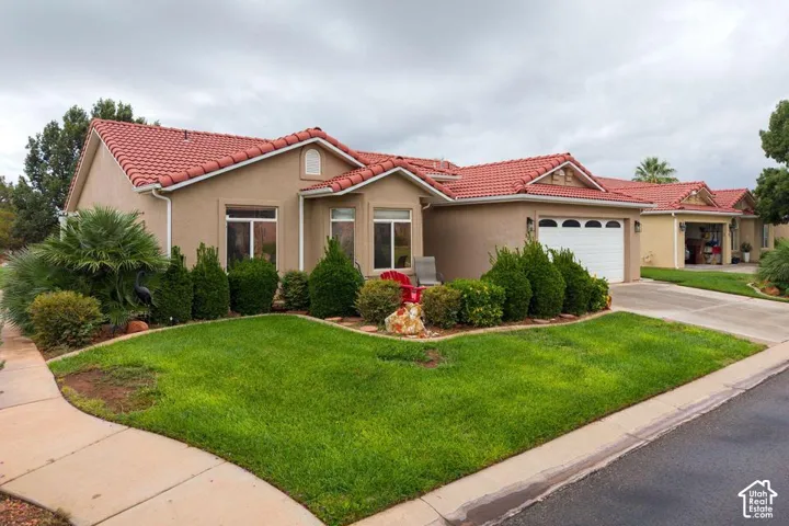Stucco exterior residence featuring a red tile roof, multi-gable roofline, arched garage door detailing, and manicured landscaping
