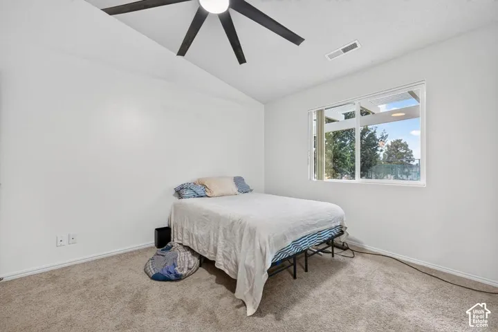 Vaulted ceiling featuring a central multi-blade ceiling fan, wall-to-wall carpeting, and a large window with exterior landscape exposure