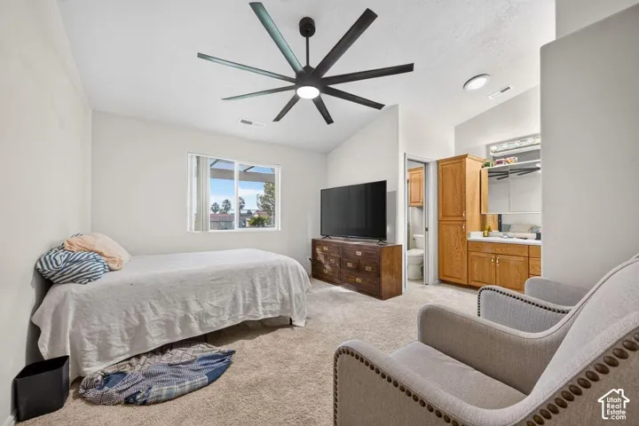Vaulted ceiling with a multi-blade matte black ceiling fan, recessed lighting, wall-to-wall carpeting, and wood-finish cabinetry with a built-in countertop vanity