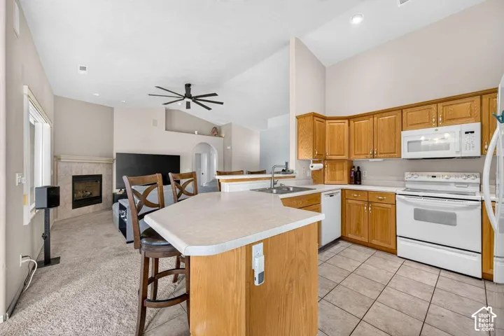 Kitchen featuring oak cabinetry, laminate countertops, a peninsula, and tile flooring, paired with a living area containing a tile-surround fireplace and vaulted ceilings