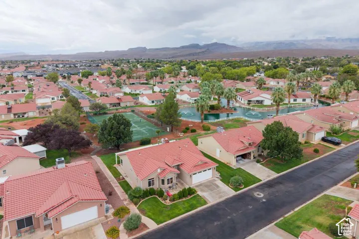 Aerial perspective of a residential neighborhood featuring clay tile roofing, paved streets, manicured landscaping, and mountain backdrops