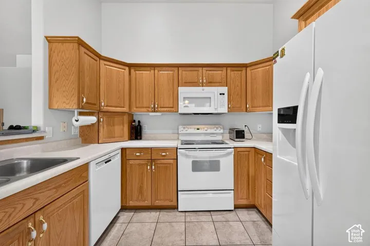 Kitchen featuring natural wood cabinetry, white appliances, a solid-surface countertop, and tile flooring