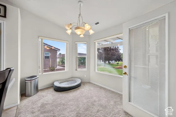 Corner room featuring expansive bay windows, carpeted flooring, a multi-arm chandelier, and a full-lite exterior door with integrated blinds