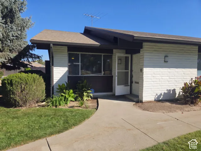 Exterior featuring painted brick siding, low-pitch roofline with exposed beams, large picture window, and concrete walkway