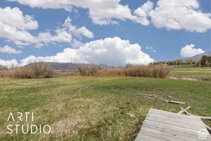 Expansive open acreage featuring native grasses, mature shrubbery, a wood-plank footbridge, and mountain backdrop