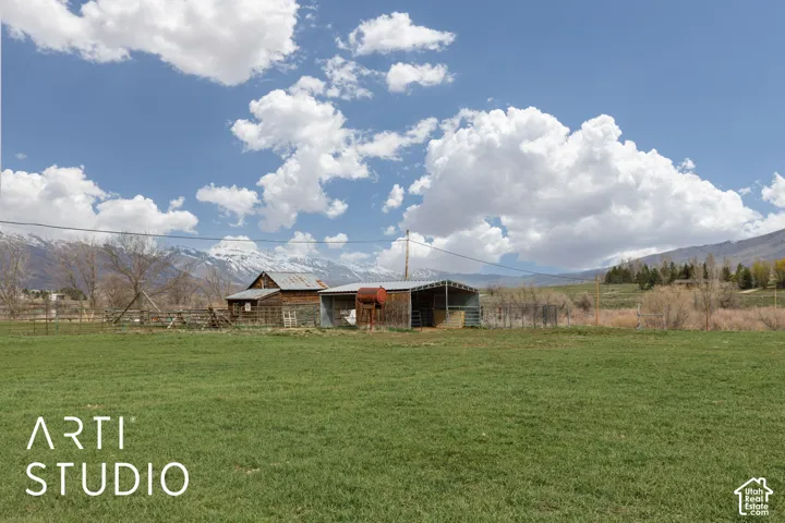 Expansive acreage featuring a weathered wood-sided barn, metal-roofed animal shelter, wire fencing, and mountain backdrop