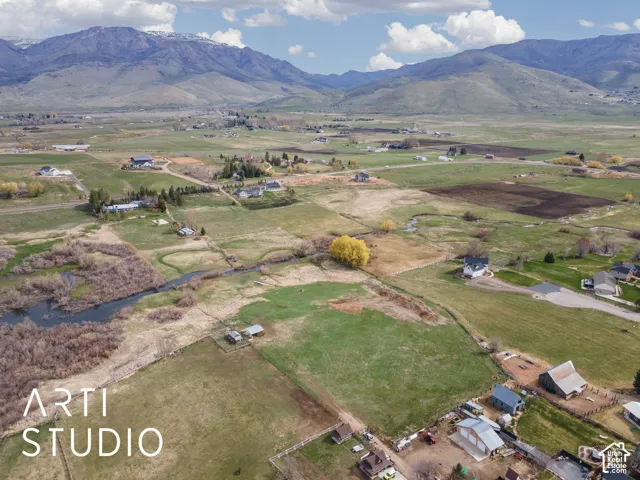 Aerial perspective of expansive acreage featuring vast open pastures, a natural water feature, and a prominent mountain range backdrop