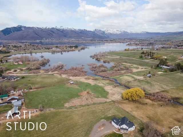 Aerial perspective of expansive acreage featuring open pasture, mature trees, water frontage, and mountain backdrop