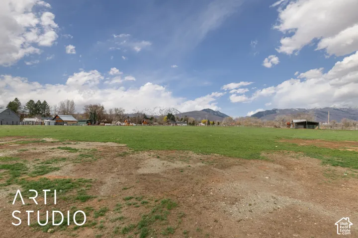 Expansive acreage featuring a broad grass field, structures, and a mountain backdrop