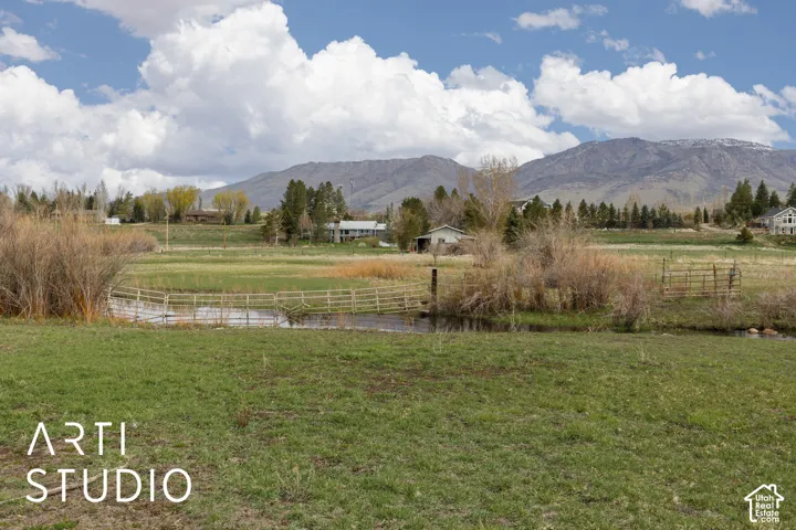 Expansive parcel featuring open pasture, a natural waterway, split-rail fencing, and mountain scenery