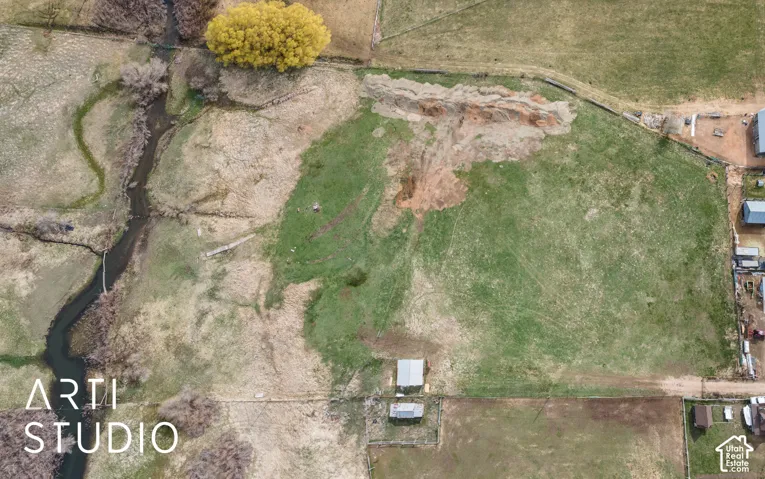 Aerial perspective of expansive acreage featuring open pasture, a natural creek, and mature trees