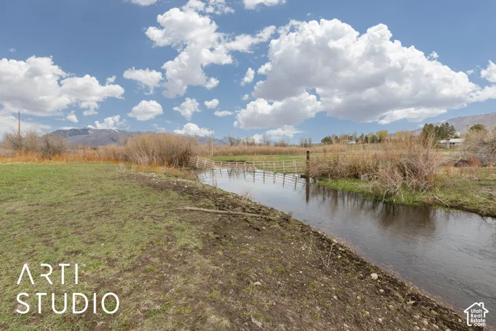Expansive acreage featuring a natural creek, mature vegetation, rustic wooden fencing, and mountain scenery