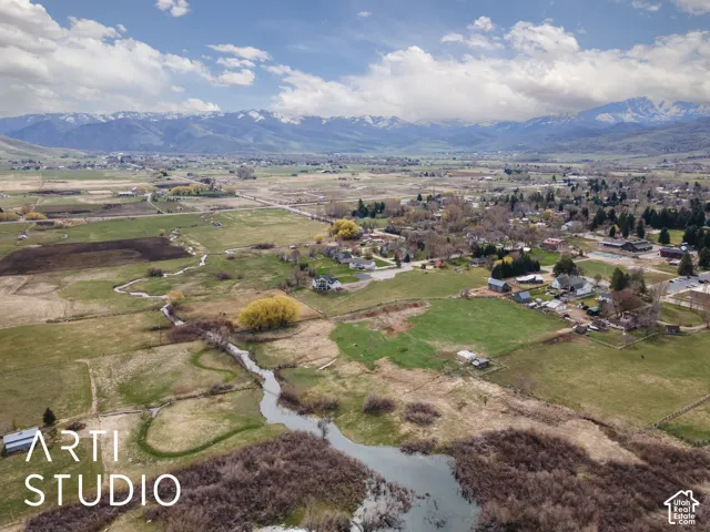 Aerial perspective showcasing expansive acreage, a winding creek, and a mountainous backdrop