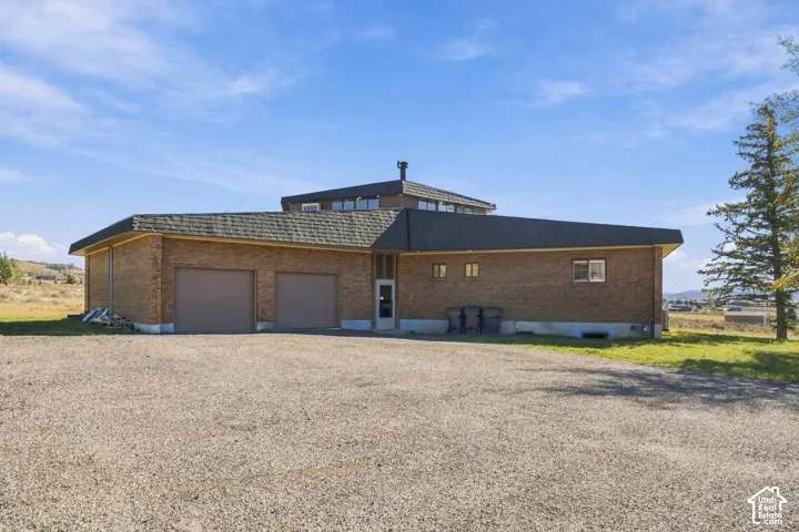 Brick exterior residence featuring a multi-level roofline, clerestory windows, and an attached two-car garage set on a gravel lot