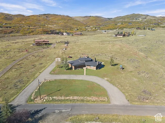 Single-story residence featuring a multi-faceted roofline, brick exterior, stone chimney, paved circular driveway, and mountainous topography