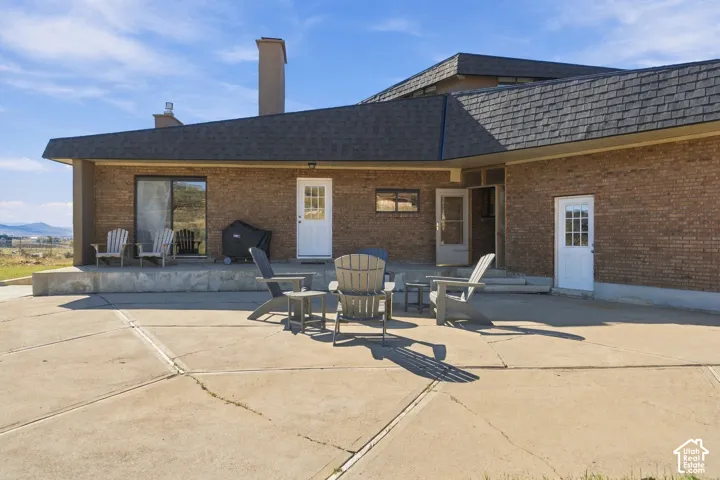 Expansive concrete patio featuring brick exterior walls, multiple points of egress, and an architectural chimney